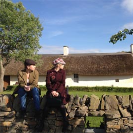 Two young women dressed as Suffragettes sit on the wall outside Burns Cottage